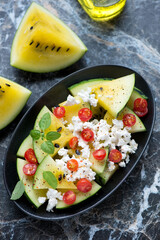 Salad with yellow watermelon, goat cheese and cherry tomatoes, vertical shot on a black marble background