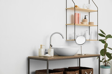 Table with modern sink and bath accessories near white wall