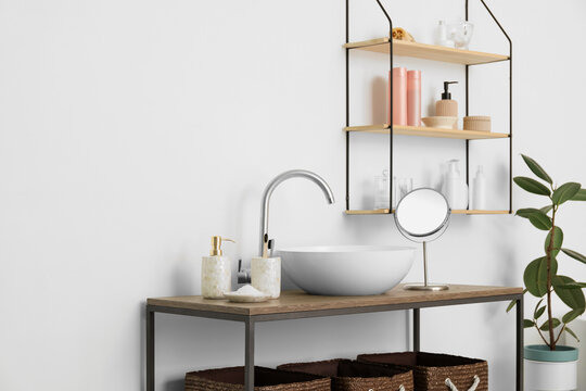 Table with modern sink and bath accessories near white wall © Pixel-Shot
