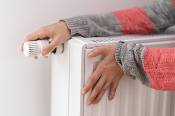 A woman touches a cold radiator of a home heater and increases the heating power