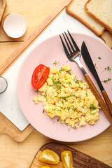 Plate of tasty scrambled eggs on wooden table, closeup