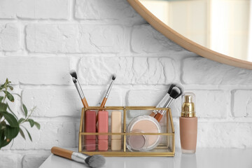 Organizer with makeup brushes and decorative cosmetics on table near white brick wall