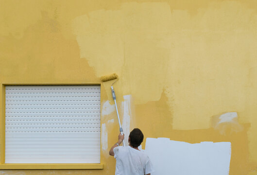 Rear view of a man painting a house yellow with a paint roller, Spain