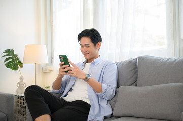 Young asian man using smart phone on sofa in living room.