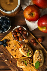 Board of tasty apple wedges with nut butter, hazelnuts and blueberry on wooden background, closeup