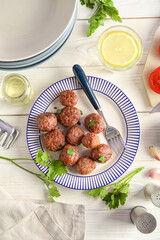 Plate with tasty meat balls, parsley, oil and glass of water on white wooden background