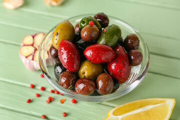 Bowl of delicious olives with spices on color wooden background, closeup
