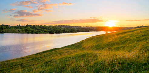 Summer sunny landscape with sun rising over the blue calm river and green hills.