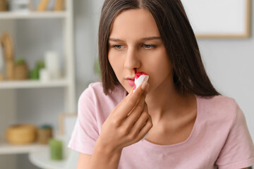 Young woman wiping nosebleed with tissue at home, closeup