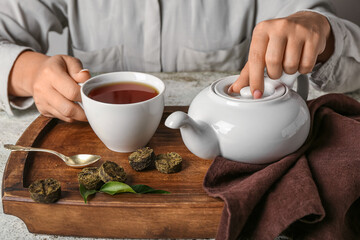 Female hands with cup of puer tea, teapot and dry pressed leaves on table, closeup