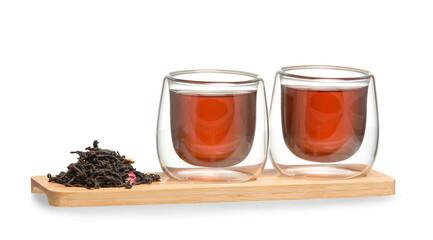 Wooden board with glass cups of black tea and dry leaves on white background