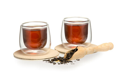 Glass cups of black tea and scoop with dry leaves on white background