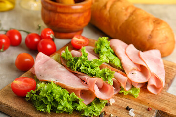 Wooden board with sliced delicious ham and lettuce on table, closeup