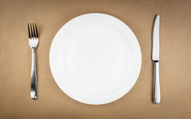 Empty plate with fork and knife isolated on brown recycled paper background with copy space