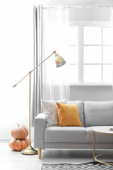 Autumn interior of living room with grey sofa, lamp and pumpkins