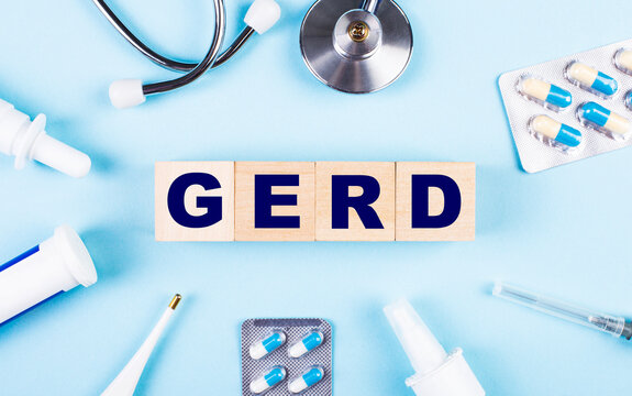 On a blue background, a stethoscope, a thermometer, other medicines and wooden cubes with the text GERD. View from above. Medical concept