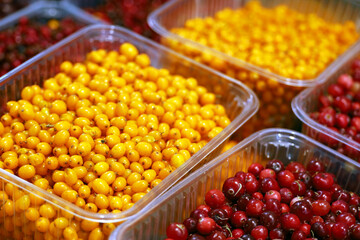 Naklejka na ściany i meble Fresh sea buckthorn and cranberry berries in plastic containers. Fresh autumn harvest in a store