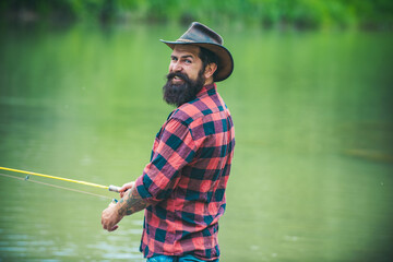 Portrait of young man fishing. Fisherman with rod, spinning reel on river bank. Man catching fish, pulling rod while fishing on lake. Wild nature. The concept of rural getaway.