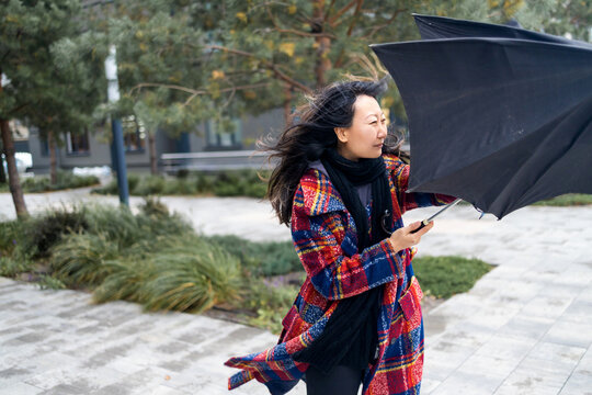 Woman Trying To Hold Her Umbrella In Strong Wind