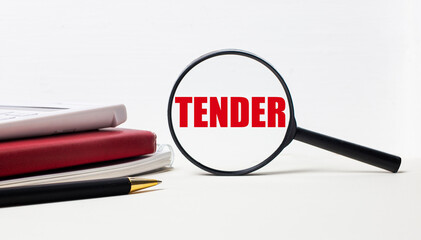 Office table with notepads, black calculator, pen and magnifying glass with TENDER inscription. Side view.