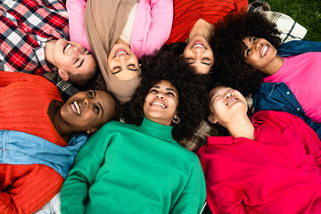 Happy young multi ethnic women having fun lying on park grass - Diversity and friendship concept
