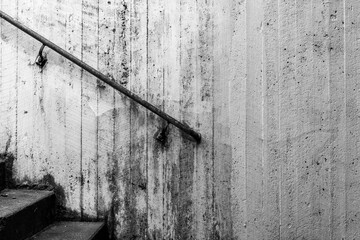 Concrete wall and part of stairs and handrail in gritty black and white. No visible people