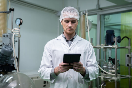 Male scientist, apothecary working in a laboratory for cannabis extraction while carrying a tablet containing extracted chemistry data from hemp leaf and cannabis plants. Medicinal cannabis extraction