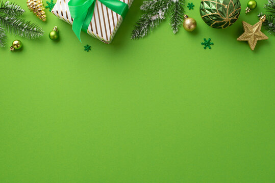 Christmas concept. Top view photo of big giftbox gold and green baubles pine cone star ornaments confetti and spruce branches in hoarfrost on isolated green background with copyspace