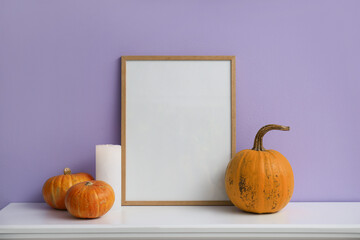 Blank frame with Halloween pumpkins and burning candle on mantelpiece near lilac wall