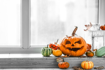 Halloween pumpkins with fallen leaves, spiders and lantern on windowsill in room