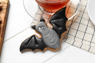 Halloween bat cookie with cup of tea and napkin on white wooden background, closeup