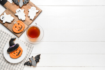 Board with Halloween cookies, plate, napkin and cup of tea on white wooden background