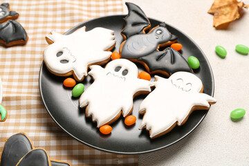 Plate with Halloween cookies and candies on white background