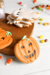 Board with Halloween cookies and candies on white wooden background, closeup