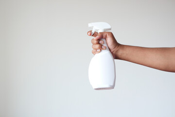 holding a white color disinfectant spray bottle against white wall  - obrazy, fototapety, plakaty