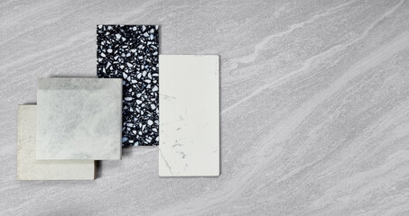 top view of interior material samples contains gloss and matt grey tiles, black and white terrazzo artificial stone, white marble quartz placed on grey travertine background. interior material board.