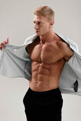 sexy muscular man in a blue shirt on a light background. Blond-haired male bodybuilder.