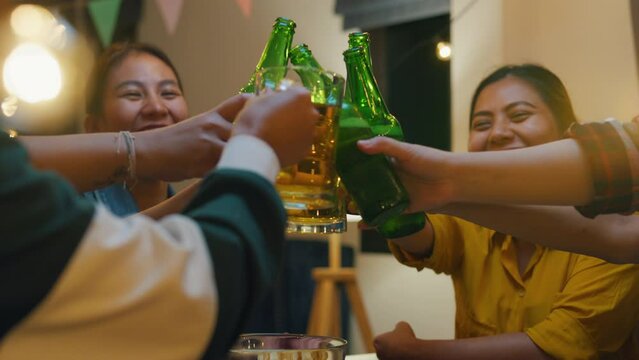 Group of multiethnic young adult Asia friend drinking alcohol beer bottle glass and having fun laugh enjoy hangout party in night life indoor home. Happy hour time millennial generation inside house.