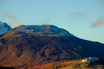 Obraz premium Lonely hotel on a hill looking down on Ushuaia, Argentina. Late sunlight enlightens the autumn forest.