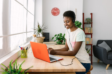 Young african woman with headset working from home office. Young woman using video chat on laptop....