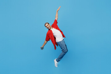 Full body side view young man of African American ethnicity 20s he wear red shirt stand on toes with outsretched hands leaning back dance on party isolated on plain pastel light blue cyan background.