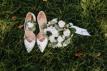 The bride's bouquet and women's shoes stand on the green grass close-up. wedding photography.