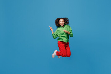 Fototapeta na wymiar Full body young woman of African American ethnicity 20s she wear green shirt jump high point index finger aside on workspace area mock up isolated on plain blue background. People lifestyle concept.