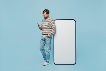 Full body young man 30s wear sweater stand near big huge blank screen mobile cell phone with...