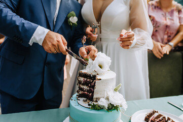 The bride and groom cut the sweet, delicious wedding cake, which is on the table, into a piece with a knife at the ceremony.