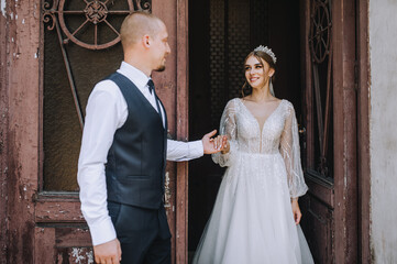 A stylish groom in a blue suit and a beautiful young bride in a white dress with a diadem on her...