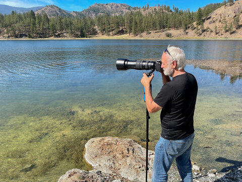 Photographer standing on the beach using a telephoto lens and tripod, Okanagan, British Columbia, Canada