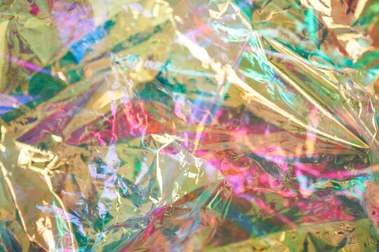 Abstract fashion rainbow holographic background in the style of the 80s. The texture of the foil with scratches and irregularities. Crumpled iridescent foil of real texture. High quality photo