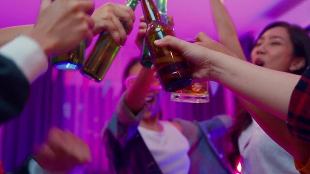 Closeup hands multiethnic young adult Asia friend wear futuristic neon glowing glasses dance and drink alcohol beer fun hangout party in living room night indoor home. Disco lights illuminating house.