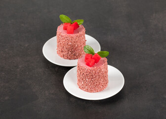 Vegan dessert. Red plum mousse cream cake of cylindrical shape, on a plate. Dark grey background